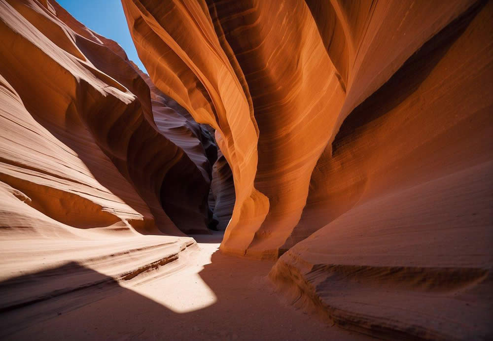 Sunlight streams through the narrow slot canyon, casting dramatic shadows on the smooth, swirling sandstone walls. The vibrant red and orange hues of the rock formations contrast with the deep blue sky above